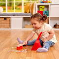 Little girl sitting on the floor and mopping glitter into the tray while using Montessori cleaning set. 
