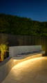 Outdoor seating area with curved concrete bench illuminated by warm LED strip lighting beneath the seat.