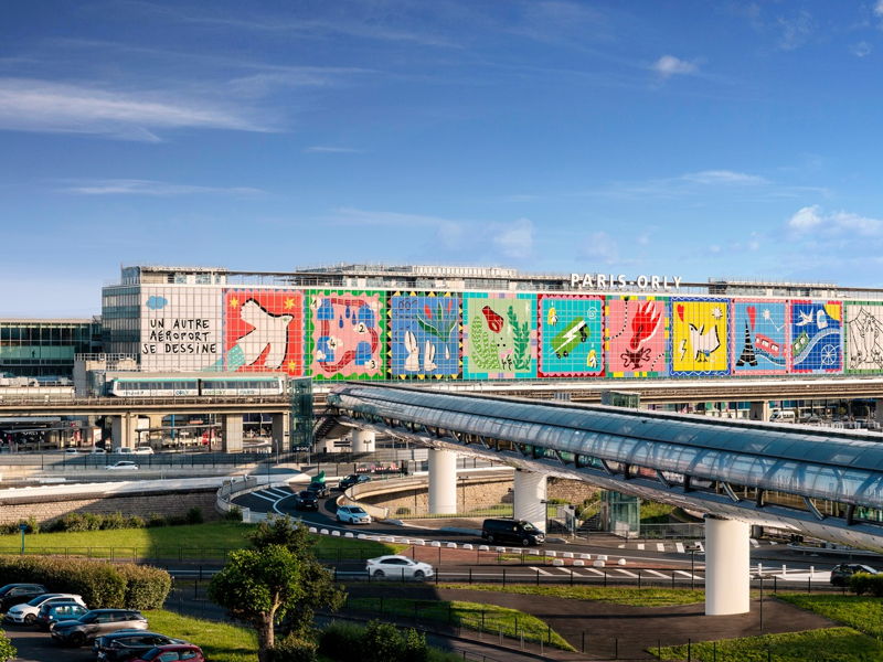 Vue panoramique de l'aéroport d'Orly montrant sa façade artistique colorée, la tour de contrôle et la passerelle de liaison