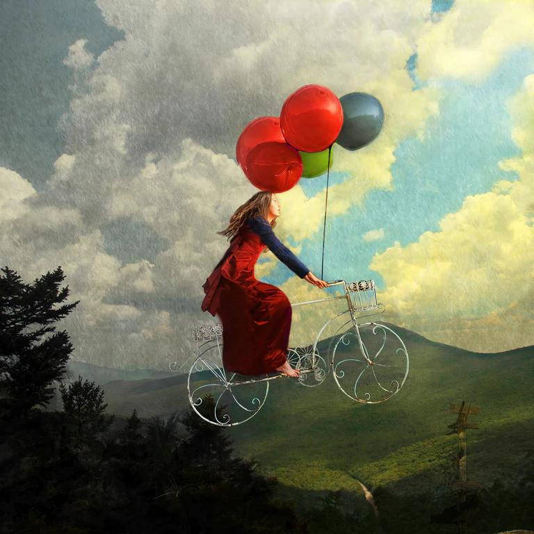A woman pedaling a bike into the air. Balloons are tied to the handlebars.