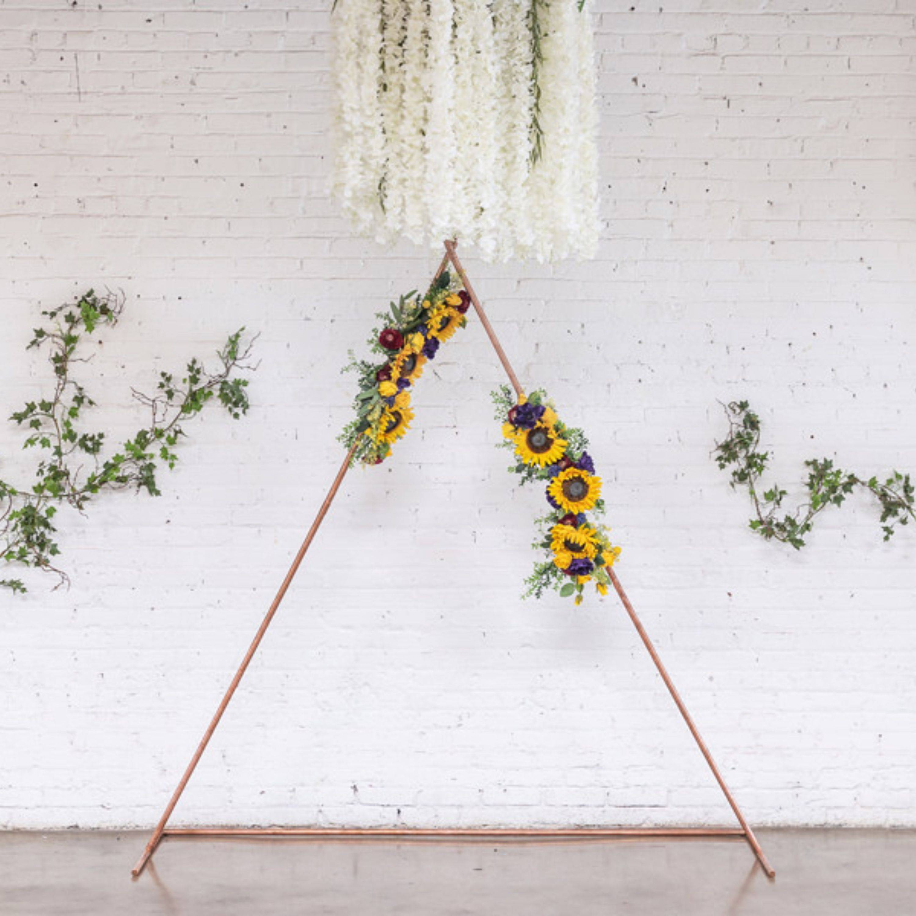 Sunflower arrangements decorate Compass Rose Floral's copper triangle wedding arch 