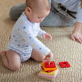 Baby playing with a wooden stacking toy next to her mom.