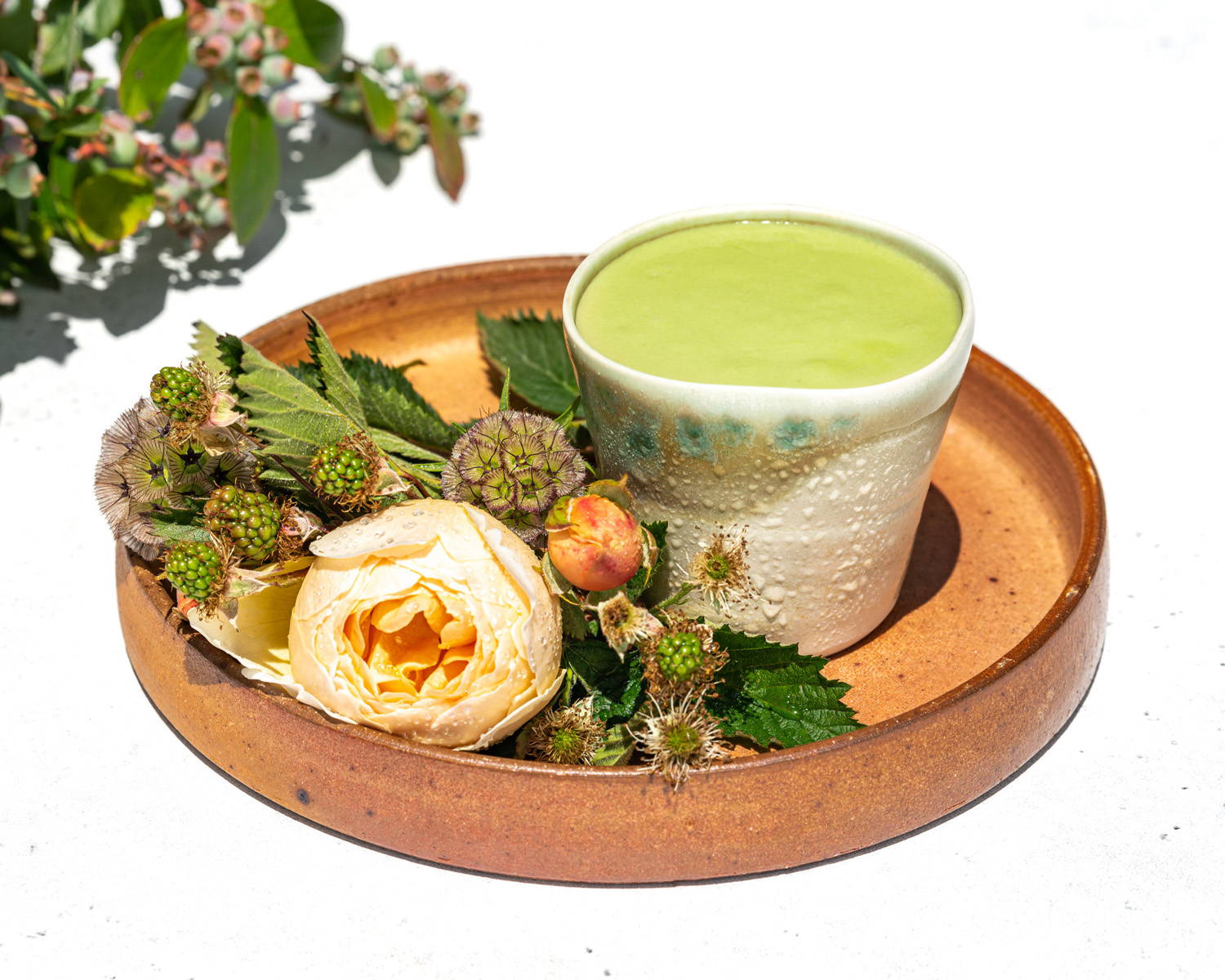 A smooth matcha mango lassi, cool with condensation on the outside of the ceramic cup, surrounded by a summer bouquet.