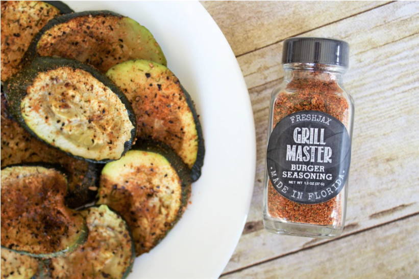 A plate loaded with grill master zucchini next to a sampler size bottle of FreshJax's Organic Grill Master Seasoning.