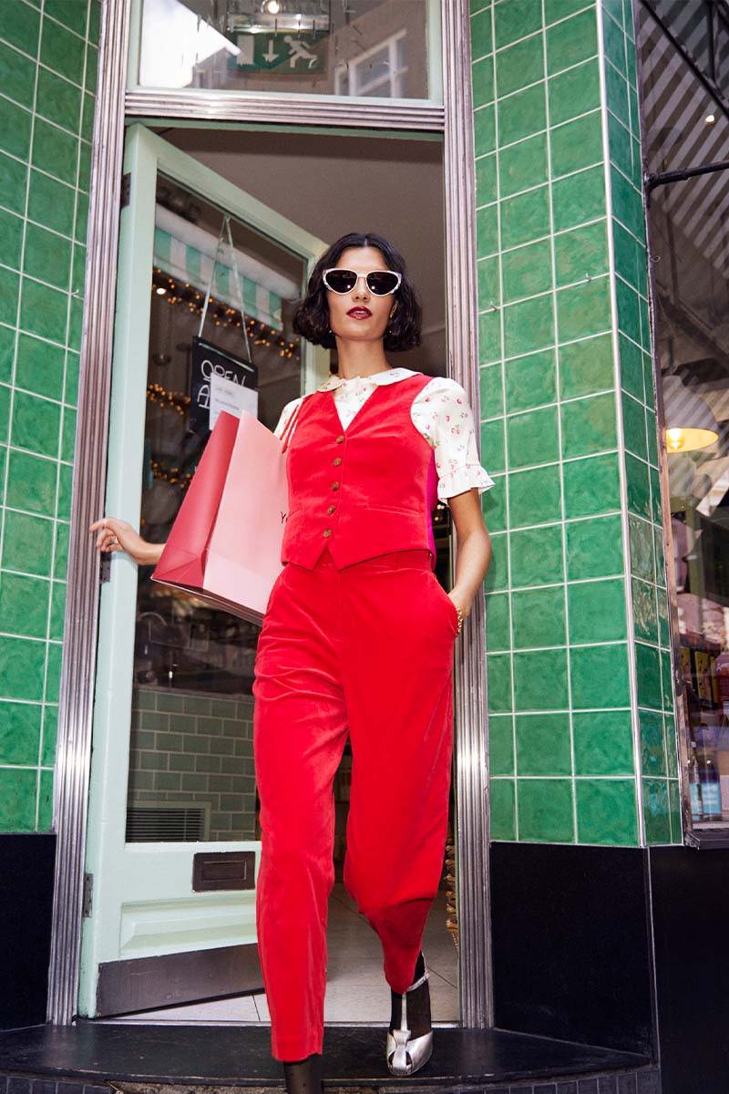 A girl wearing YOLKE's Love Suit in Cherry Red Corduroy steps out of a store in SoHo London