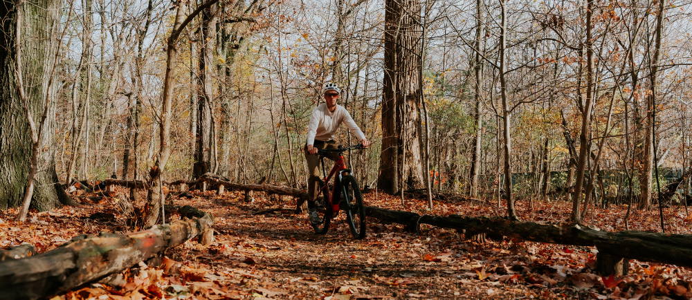 A man riding an electric mountain bike on a leaf covered path in the forest