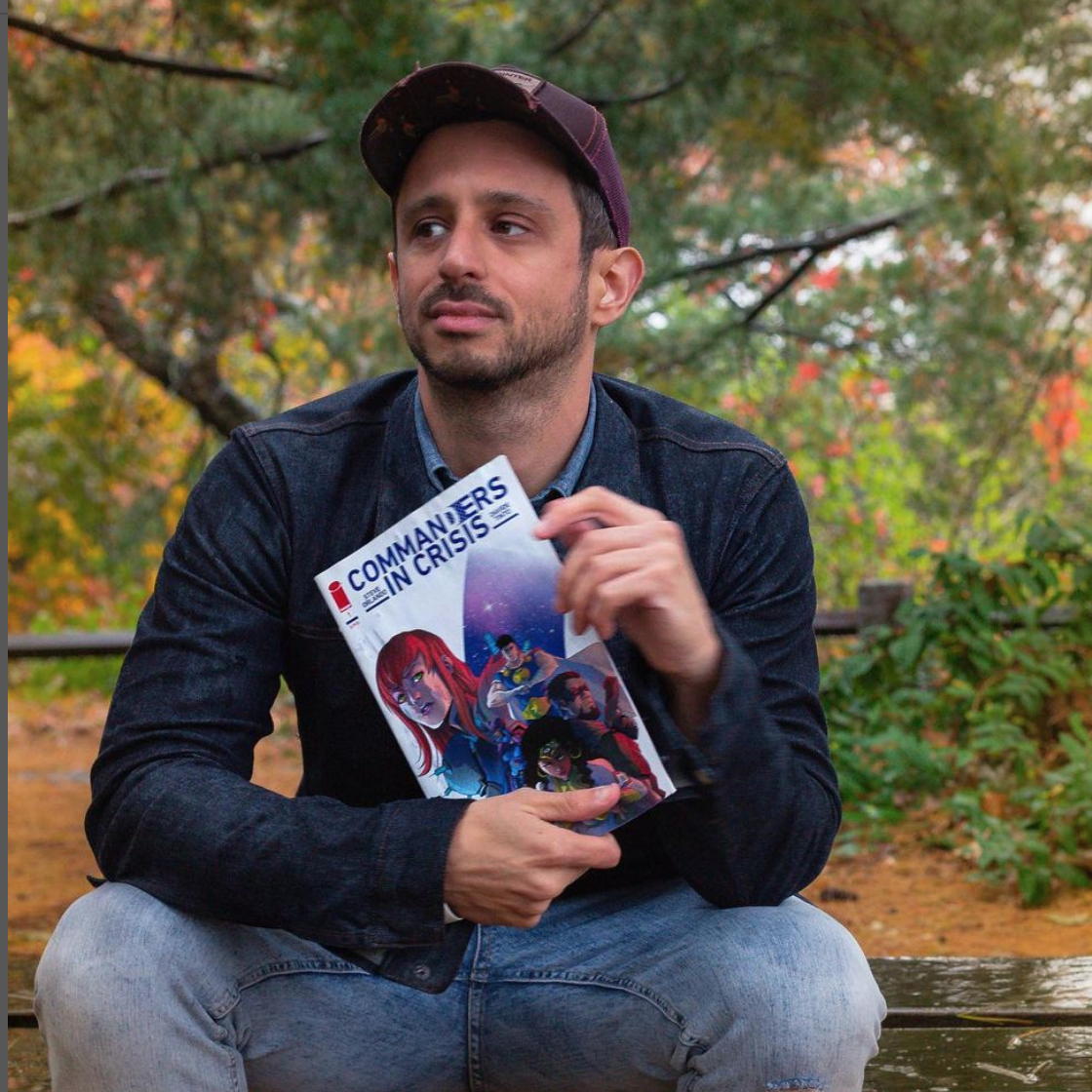 Steve Orlando sitting on a bench outdoors with a comic in his hands while he looks to his side.