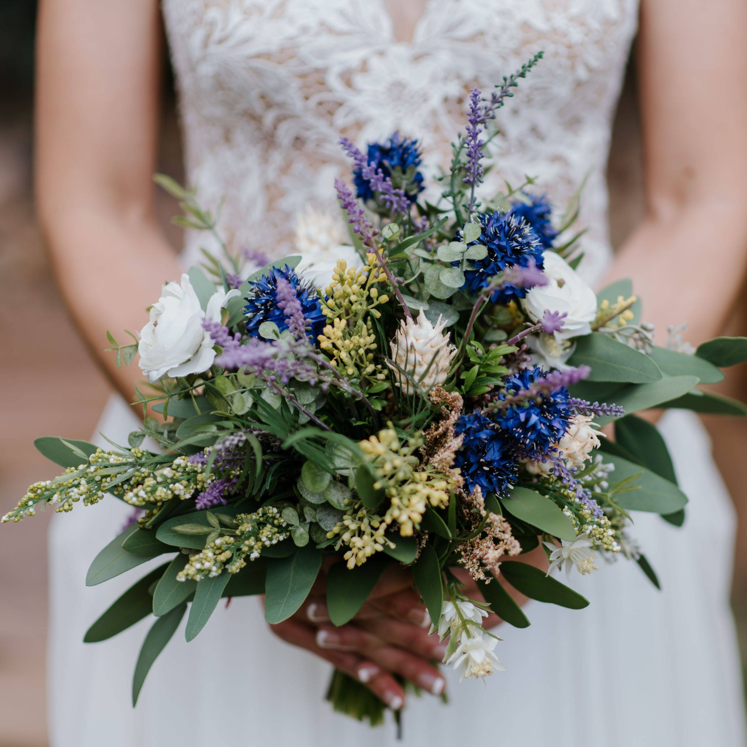 Wildflower bouquet with lush greenery, blue, lavender, and white flowers 