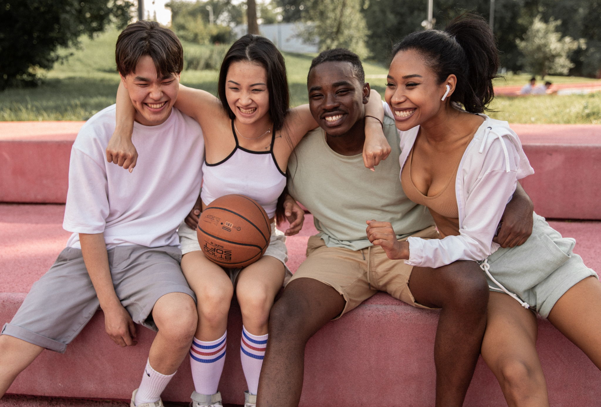A group of mixed friends sitting together and hugging with sportswear and a basketball.