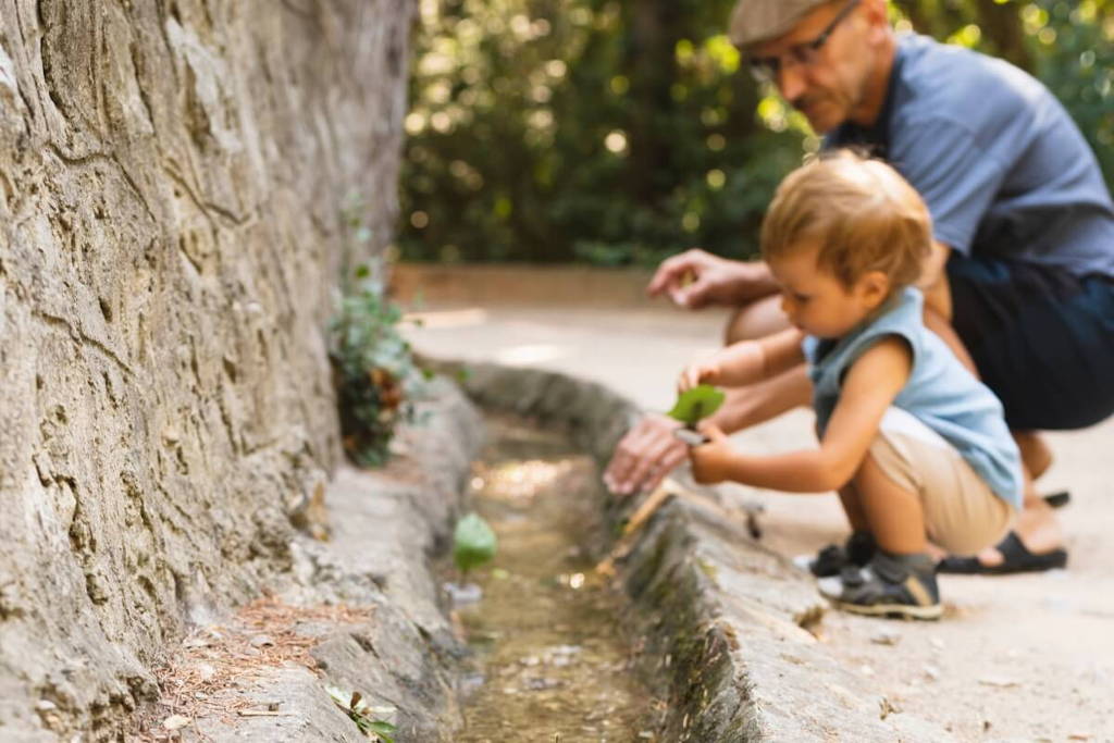 Grandparent and grandson crouching next to a small creek.