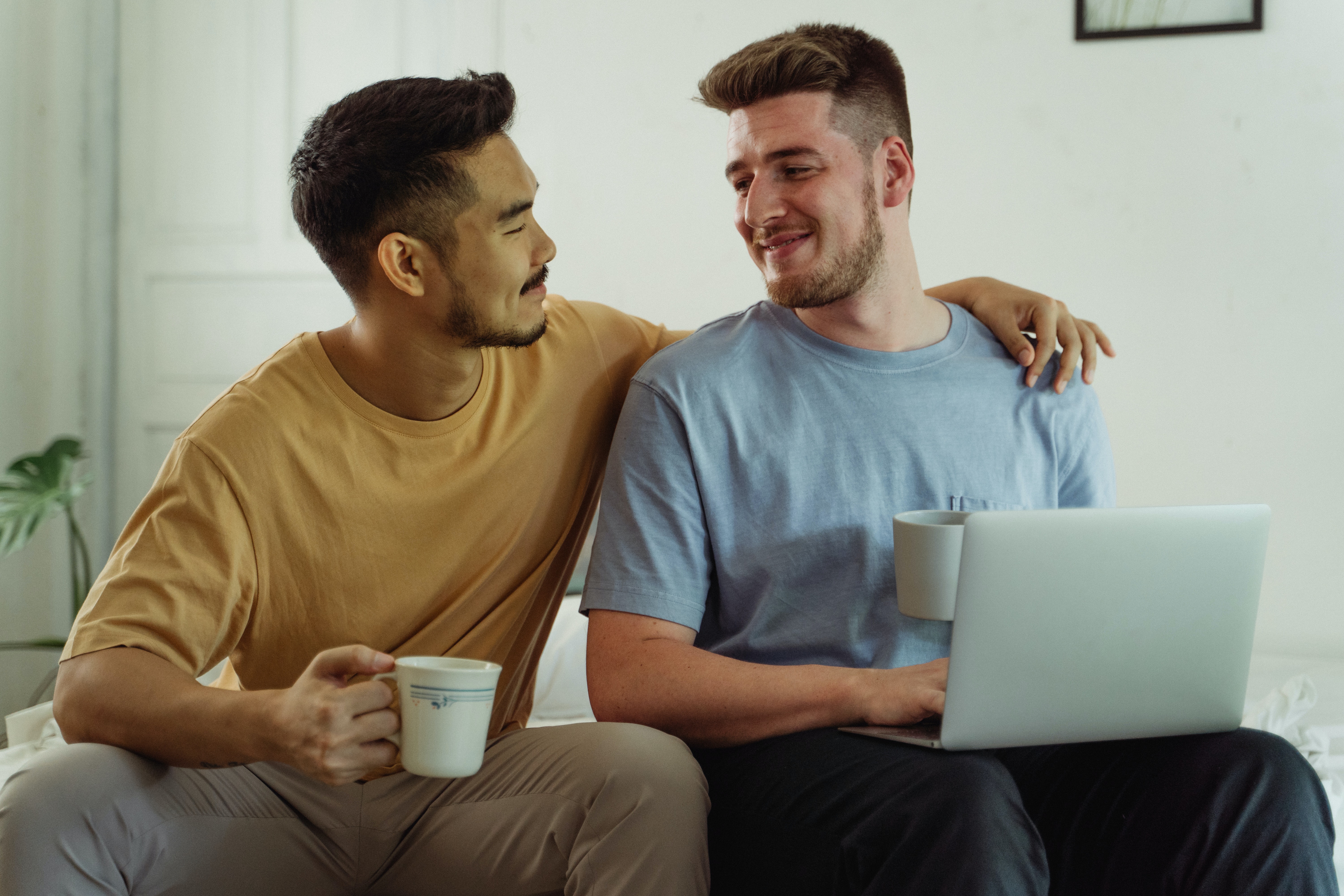 An asian and white man having an intimate moment drinking coffee and smiling to eachother.