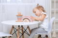 A little girl sitting on a chair and playing with different Montessori toys on the table. 