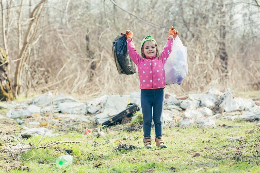 Little girl holding bags of litter that she collected in the woods.