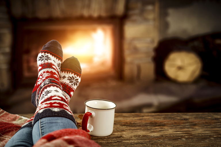 thick and cozy winter socks up on a table next to a coffee mug and in front of a warm fire