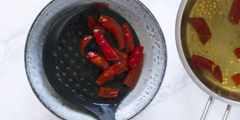 Place the strainer/colander of boiled dried chillies in another bowl of clean water to further remove excess seeds.