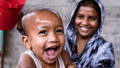 an image of a baby boy smiling and laughing as his mother pours clean water over his head.