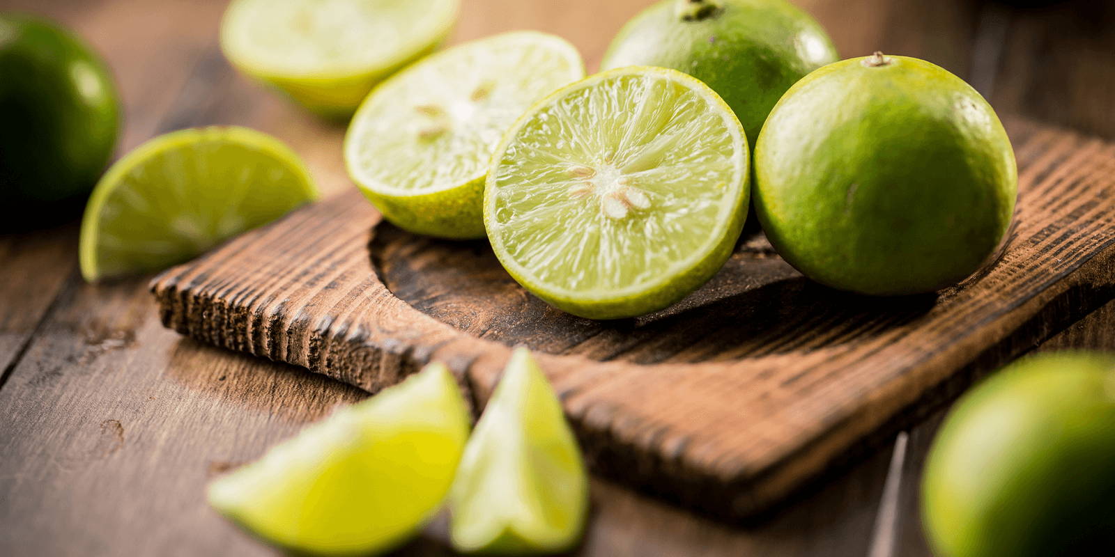 Halved, quartered, and whole limes, placed on a wooden board.