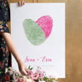 woman holding fingerprint heart canvas guest book on easel with flower bouquet