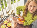 Child squeezing fresh oranges during a summer-themed sensory play activity.