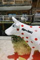 Statue d'une vache décorée avec le maillot à pois rouges du Tour de France, devant un chalet de montagne