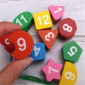 A hand holding an orange wooden piece while the rest of the colorful Penguin's Clock parts are lying on the table beneath. 