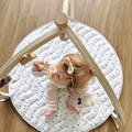 Baby sitting on her Montessori Baby Play Mat and playing with hanging mobile toys.