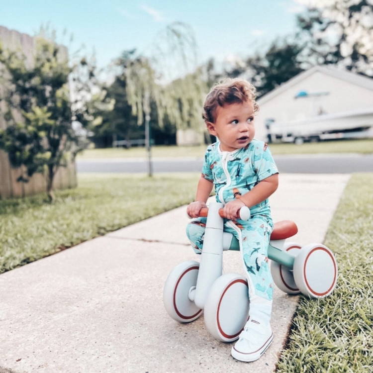 Little boy in cute blue outfit sitting on a Montessori Baby Balance Bike.