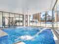 Moderner Indoor-Whirlpool mit Massagedüsen und großen Glasfenstern, die einen hellen Blick auf den Außenpool und Palmen bieten.