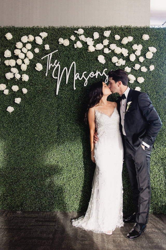 Newlyweds in front of boxwood wall with custom sign