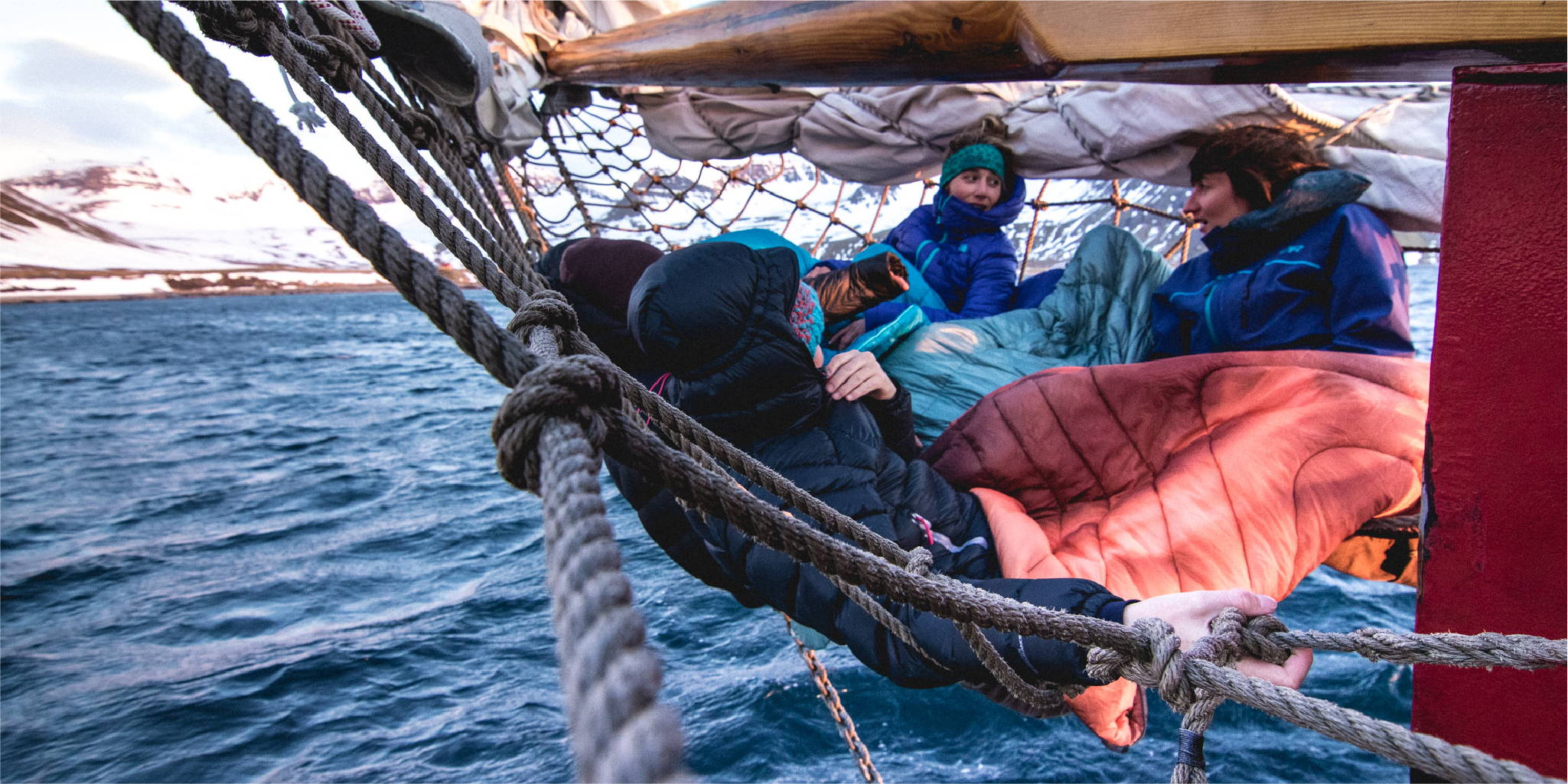 Group of three sitting on the front of a sailboat wrapped in Rumpl blankets