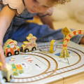 Baby girl playing with a festive Montessori Christmas Railway toy with figurines, cars, and a a box.