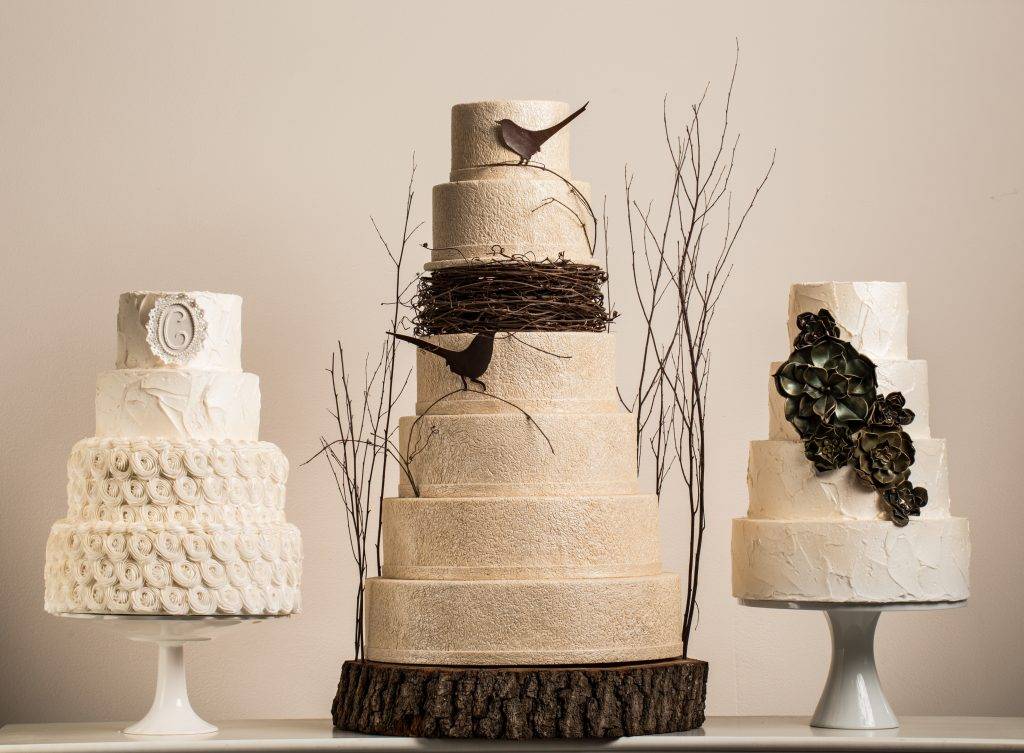 Three large wedding cakes designed by the House of Clarendon in Lancaster, PA. The center cake features a bird's nest design and all three cakes feature off-white buttercream and fondant icing.