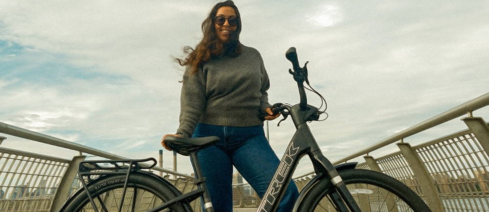 a woman standing on a bridge in new york city behind a trek electric city bike