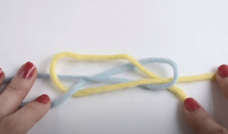 Two strands of yarn tied together with a fisherman's knot, ready to be trimmed