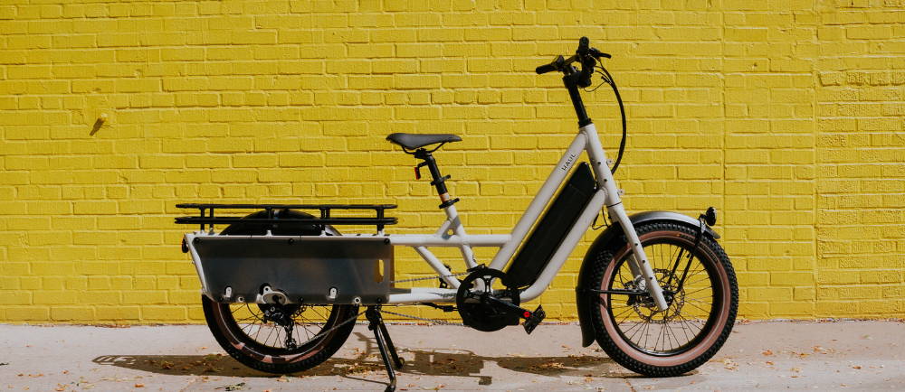 a white specialized globe haul electric cargo bike in front of a yellow brick wall