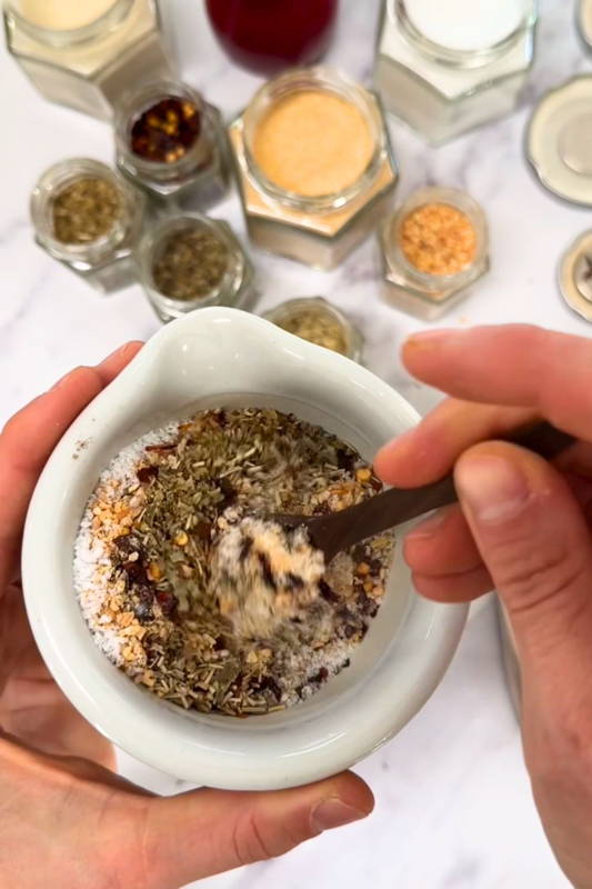 A mixture of spices being mixed to combine with many glass spice jars beneath it