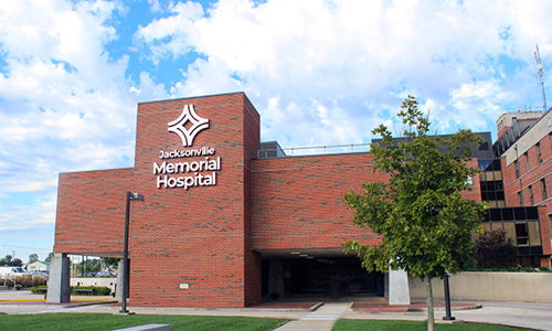 Modern "Memorial Hospital" building with large windows, trees, and a walkway, evoking hope and care amidst health concerns.