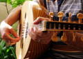 An adult male playing the electric guitar and reading tablature with the help of his private instructor.