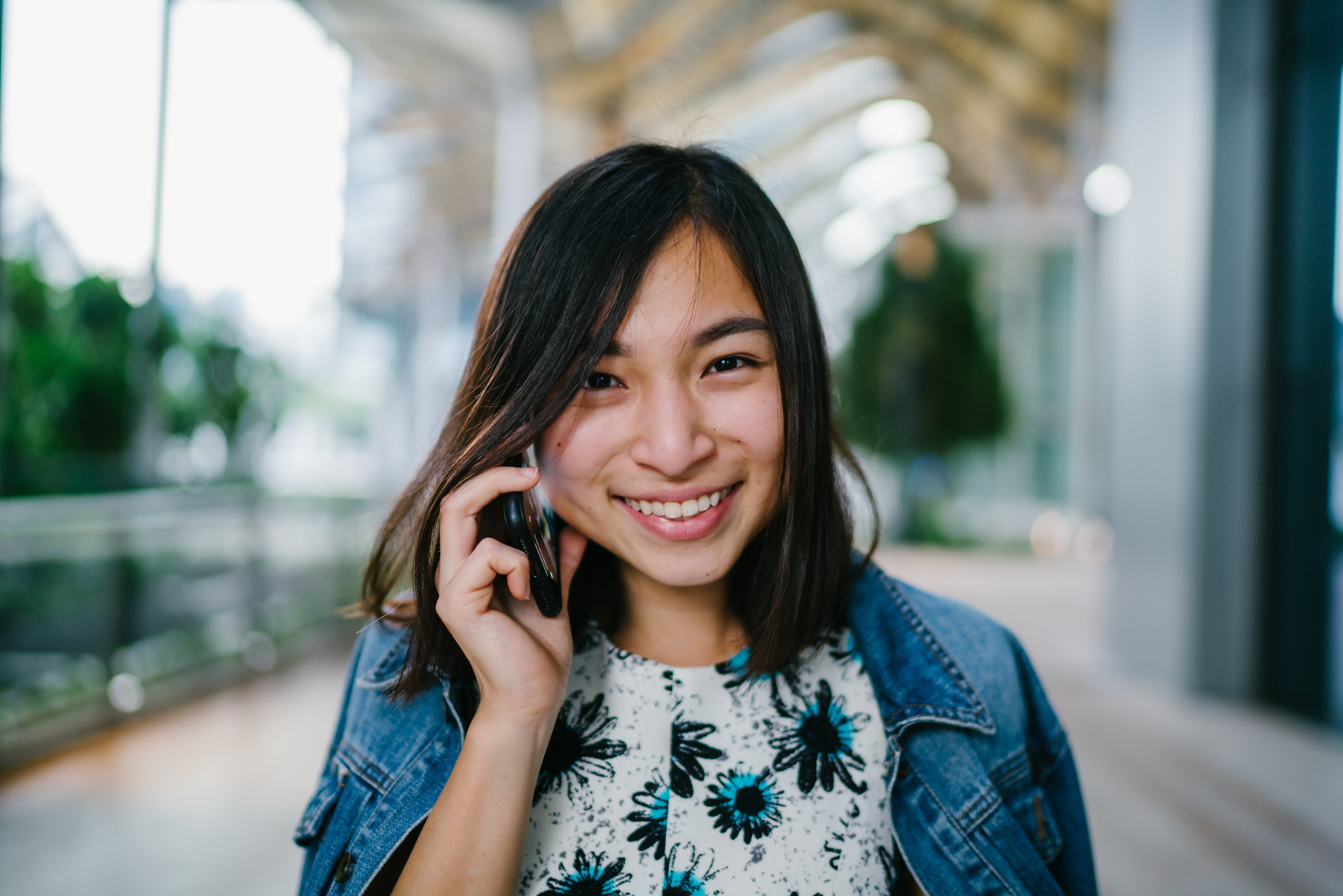 A young womman smiles while she is talking on the phone and walking on a campus.