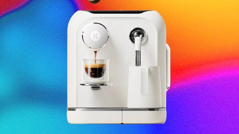 White coffee machine with a glass of espresso being filled and a container of milk being filled. A disc-shape of compact coffee floats above.