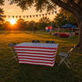 rectangular spandex tablecloth with an american flag outdoors on a table in a park with four chairs and a sunset in the background