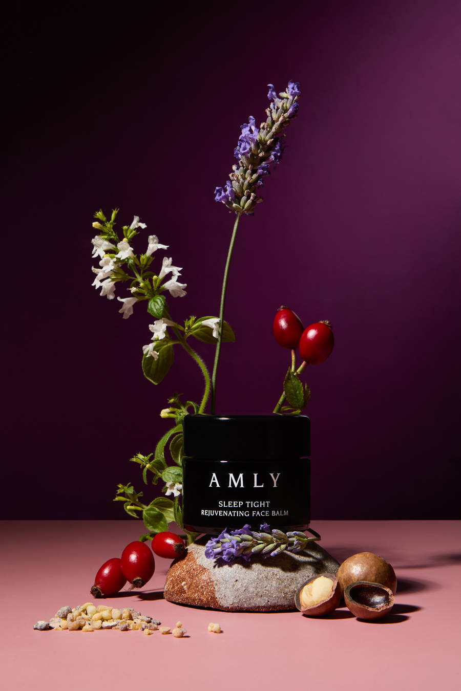 AMLY Sleep Tight balm surrounded by flowers and seeds on a dark purple background