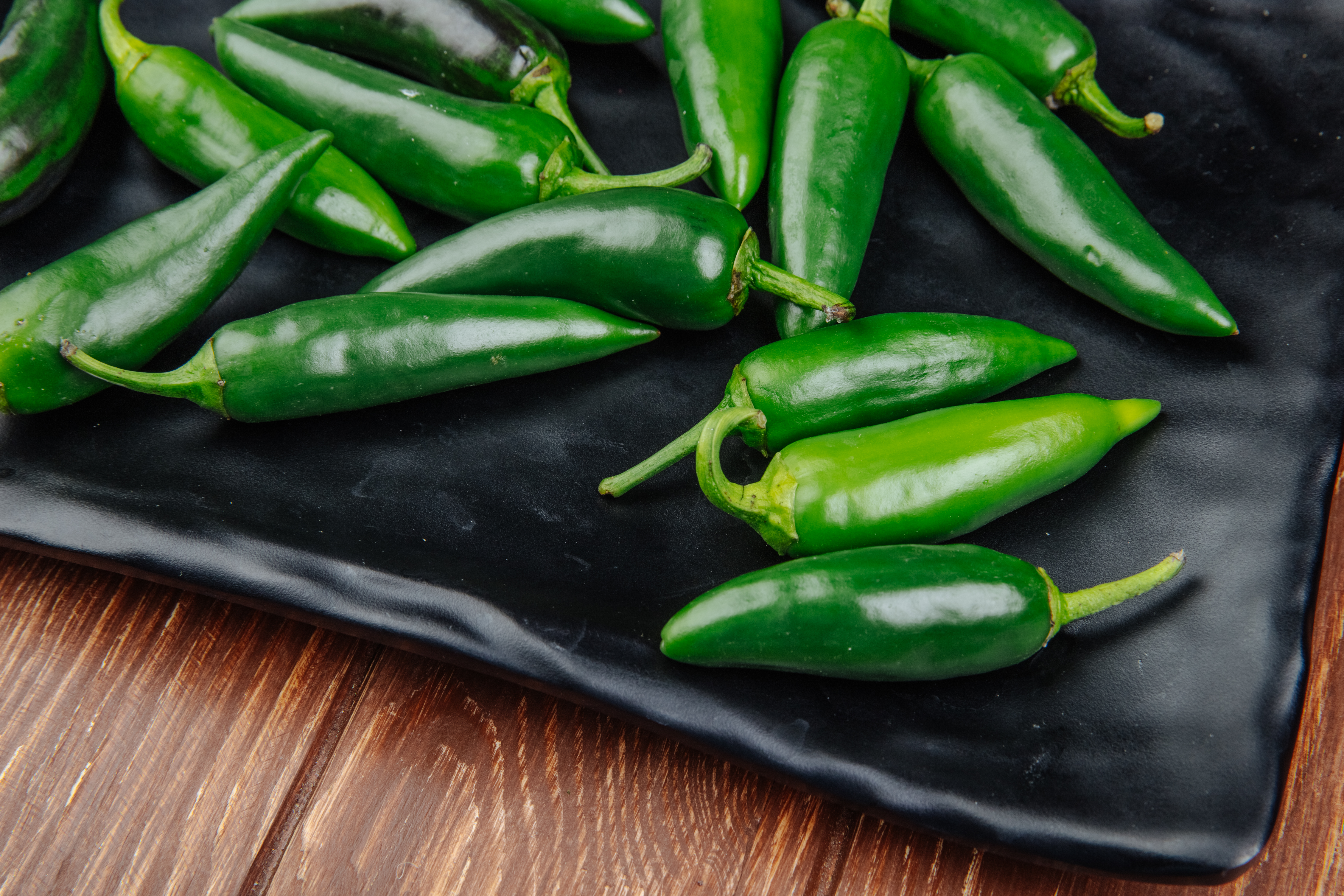 Green jalapeno peppers on a black dish with a wooden background