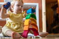 Toddler girl in a yellow dress playing with the stacking Rainbow toy.