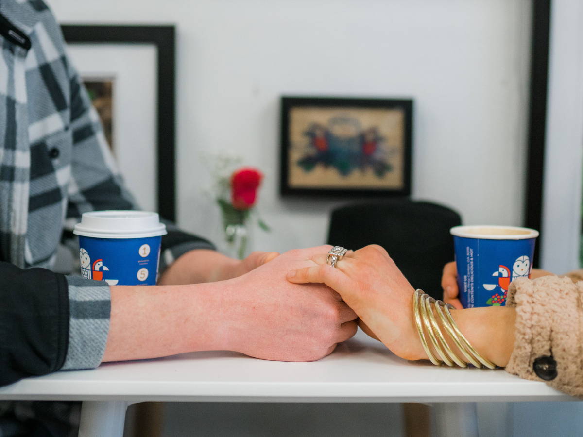 Hands holding on a table beside a flower vase.
