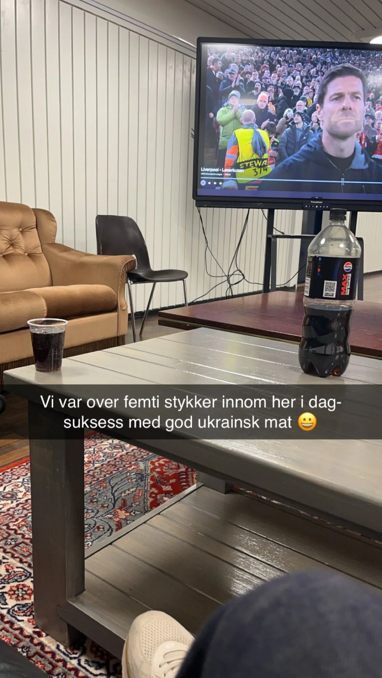 Eit snapchat-bilde tatt frå den eine sofaen. Det er tekst på bildet der det står "Vi var over femti stykker innom her i dag. Suksess med god ukrainsk mat! Smilefjes". Det står ein pepsi max på bordet, og i bakgrunnen ser ein at det er fotball på TV.