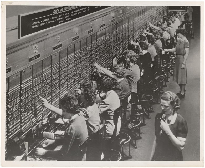 Around 20 switchboard operators working with a huge old telecommunication machine