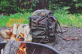 summit expedition pack resting on the ground next to some firewood and a firepit in the woods.