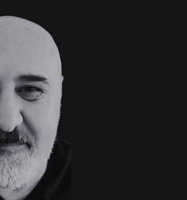 Black background with a photo of half of Chef Davide's face on the left side, in black and white. He has a small smile on his face, a bald head and a short beard and moustache. 