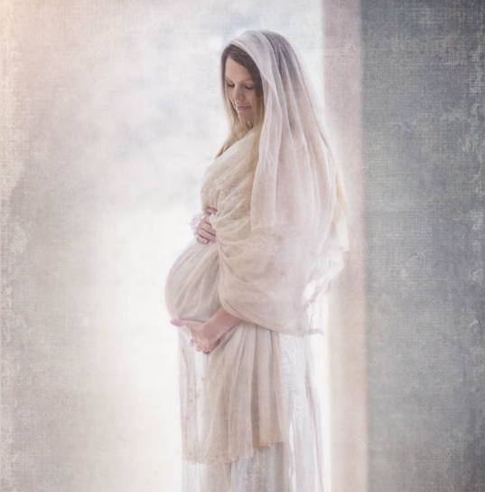 Mary wearing white and looking down at her pregnant stomach with a calm smile.